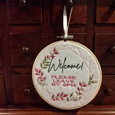 an embroidered welcome sign hanging from a wooden cabinet