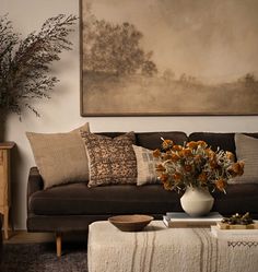 a living room filled with furniture and flowers on top of a coffee table in front of a painting