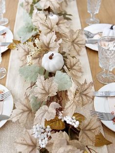 the table is set with plates, silverware and white pumpkins on it's centerpiece