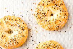 three bagels with sesame seeds and poppy seeds on a baking sheet, ready to be baked