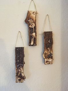 three pieces of wood hanging from hooks on a wall with mushrooms and leaves painted on them