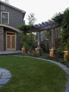 an outdoor patio with stone walkway and pergolated area in the foreground, surrounded by green grass