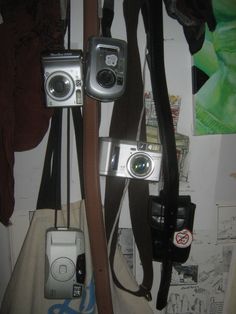 three cameras are hanging on the wall next to a purse and other items in front of them