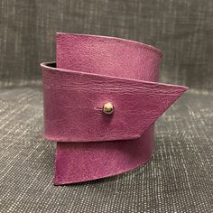 A stunning purple, Avant Garde style, leather cuff bracelet. A simplistic design and a minimalist fastening with a Sam Browne button clasp.  This cuff is lightweight and made with recycled black base leather and recycled soft leather. Size to fit wrist: Approximately up to 7 3/4 inches - 19.5cm These wrap around cuff bracelets in these colours are one of a kind. If I'm lucky enough that you would like to purchase more than one item from my shop, please contact me first so I can give you the best price postal fees.  Unique, minimal, futuristic, arty farty, arty, bold, eccentric, contemporary, modernistic. This item will be posted flat two I can keep the postal fees down. Modern Leather Cuff Bracelets, Modern Leather Cuff Bracelet, Modern Cuff Bracelet, Handmade Modern Leather Cuff Bracelet, Modern Handmade Leather Cuff Bracelet, Modern Adjustable Cuff Leather Bracelet, Modern Leather Cuff Bracelet With Wrist Strap, Unique Purple Cuff Bracelet For Gift, Purple Cuff