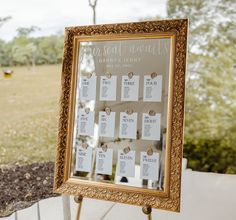 a gold framed mirror with seating cards attached to the front and back of it on a stand