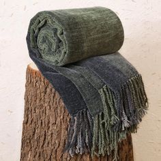 two blankets are stacked on top of each other in front of a white wall and tree stump