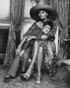 a woman sitting on top of a chair next to a little boy wearing a hat