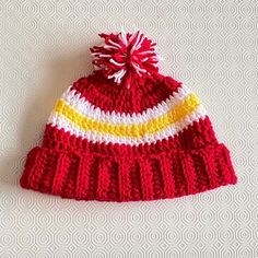 A crocheted Kansas City Chief's hat. This is the perfect hat to keep you warm whilst you watch KC play in the cold winter months.  Each hat is uniquely handmade by myself in Ireland.  If you prefer alternative colours or your favourite players number embroidered on the hat, please message me your ideas and I would be happy to custom design a hat for you.  100% soft acrylic yarn.  Available in the following sizes:  0-3 months (newborn) 3-6 months (baby) 6-12 months (baby) 1-2 years (toddler) 2-5 Nfl Hats, Hat Handmade, 6 Month Baby, Hat Crochet, Handmade Hat, White Hat, Skull Cap Beanie, Crochet Hat, Kansas City Chiefs