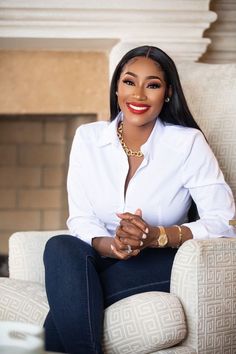 a woman sitting in a chair with her arms crossed and wearing a white shirt, blue jeans and gold jewelry