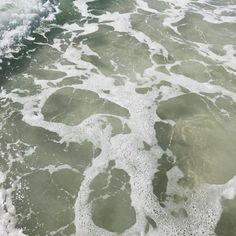 an aerial view of the ocean with white foamy water and rocks in the foreground