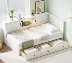 a white bed with drawers underneath it in a room next to a window and potted plant