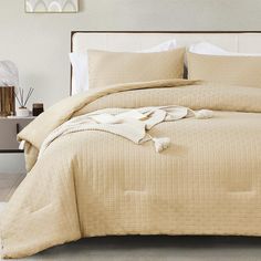 an unmade bed with beige linens and white sheets in a neutral bedroom setting