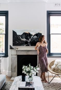 a woman standing in front of a fireplace with a painting on the wall behind her