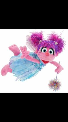 a pink stuffed animal with purple hair and blue dress on it's back, flying through the air