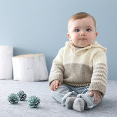 a baby sitting on the floor next to some pine cones