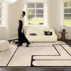 a woman walking across a living room with a white couch and black rug on the floor