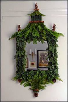 a mirror hanging on the side of a wall covered in green plants and pine cones