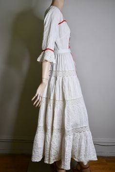 "This dress is so special. It is a vintage 60s/70s Mexican pin tucked white dress. The dress has a square neckline, that is trimmed with red ribbon and small lace ruffles, is fitted to the waist with a floral embroidered bodice that is also finished on the side with red ribbon, it has 3/4 sleeves with a flared lace cuff and red ribbon trim, The skirt is a long maxi skirt that is quite full, it has a front and back center panel with red ribbon running down the length, coming off the front panel i Bohemian Lace Dress With Broderie Anglaise, Fitted Broderie Anglaise Maxi Dress, Hippie Fitted Dress With Ruffles, White Lace Trim Maxi Dress For Festivals, Bohemian Cotton Dresses With Broderie Anglaise, White Lace Prairie Dress For Wedding, White Lace Prairie Wedding Dress, White Folk Style Wedding Dress, Fitted White Maxi Dress For Festival