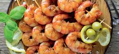 shrimp skewers with limes and olives on a wooden platter, ready to be eaten