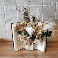 an open book with flowers and feathers on it sitting on a table next to a brick wall