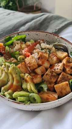 a bowl filled with tofu and vegetables on top of a bed