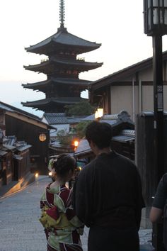 two people standing in front of a tall building with lights on it's side