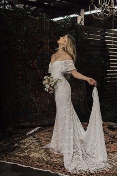 a woman in an off the shoulder wedding dress standing on a rug and looking up