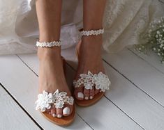 a bride's feet wearing sandals with white flowers on the toes and lace detailing