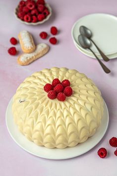 a cake with raspberries on it sitting on a table next to plates and spoons