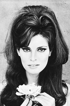 a black and white photo of a woman with long hair holding a flower in front of her face