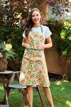 a woman standing in front of a table with an apron on and oranges on it