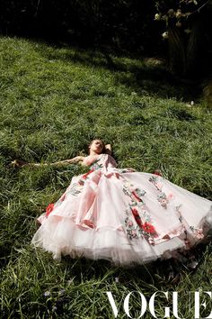 a woman laying in the grass wearing a pink and white dress with flowers on it