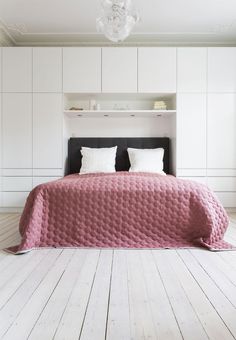 a bed sitting in the middle of a bedroom next to a white wall and wooden floor