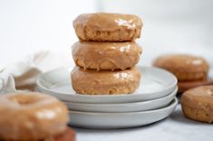 three glazed doughnuts stacked on top of each other in front of more donuts