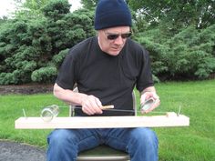 a man sitting on top of a toilet seat holding a piece of wood in his hands