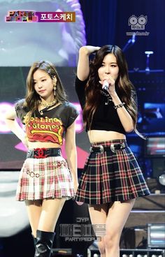 two girls are performing on stage with one holding a microphone and the other wearing a skirt