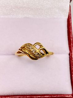 a gold ring with two diamonds in it sitting inside a red velvet box on top of a white cloth