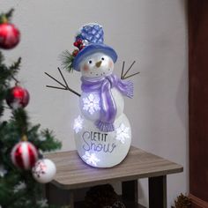 a snowman sitting on top of a table next to a christmas tree