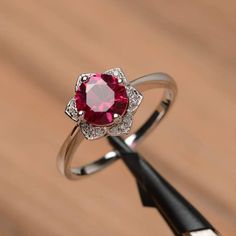 a close up of a ring with a red stone in it on a wooden table