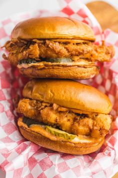 two chicken sandwiches sitting on top of a red and white checkered tablecloth covered basket