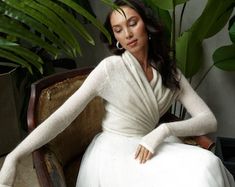 a woman in a white dress sitting on a chair next to a potted plant