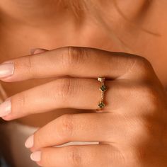 a woman's hand with a gold ring and green stones on her left finger