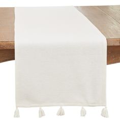 a white table runner with tassels on the edge and wooden table in the background