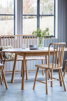 a dining room table with chairs and a vase on the table in front of two windows