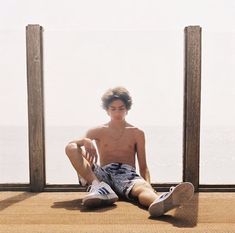 a young man sitting on top of a wooden floor next to the ocean