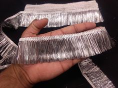 a hand is holding some silver tinsel on a black tablecloth with fringes