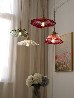 three lights hanging from the ceiling above a vase with flowers in front of a window