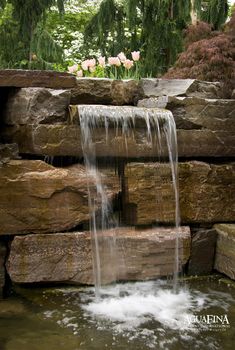 a small waterfall in the middle of a rock garden wall with water flowing from it