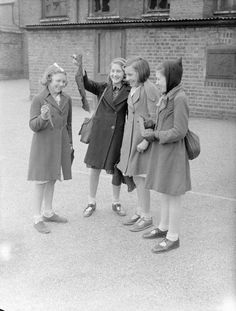 black and white photograph of four girls standing in front of a building with their hands up