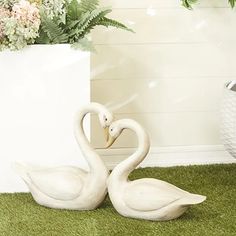 two white swans sitting on top of a green carpet next to a vase with flowers